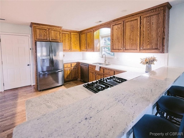 kitchen with sink, kitchen peninsula, light hardwood / wood-style floors, a kitchen bar, and appliances with stainless steel finishes