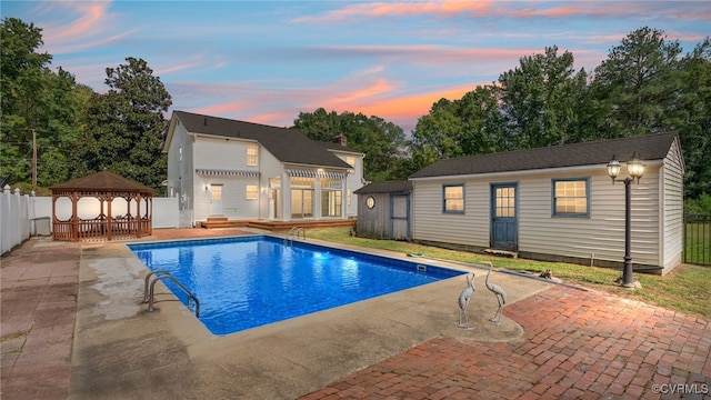 pool at dusk featuring a gazebo, a patio area, and an outdoor structure