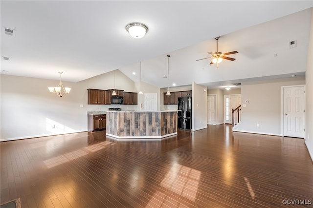 unfurnished living room with high vaulted ceiling, dark wood-type flooring, and ceiling fan with notable chandelier