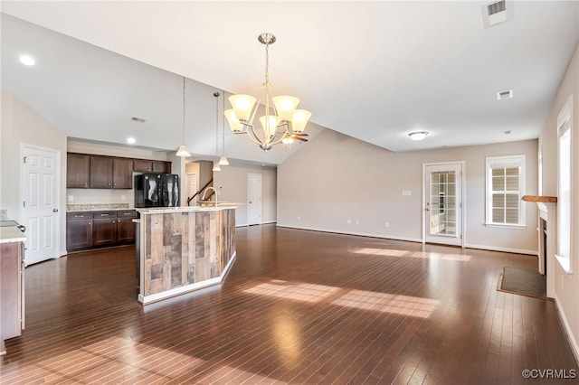 kitchen with black refrigerator, hanging light fixtures, a notable chandelier, a center island with sink, and dark brown cabinets