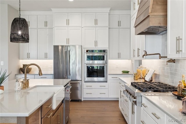 kitchen with appliances with stainless steel finishes, premium range hood, white cabinetry, and hanging light fixtures