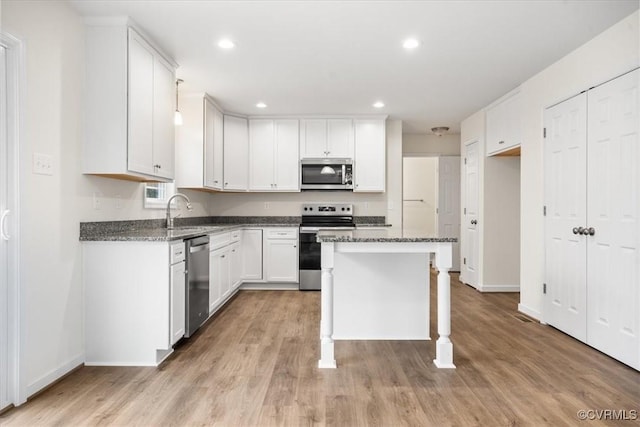 kitchen with appliances with stainless steel finishes, dark stone counters, a kitchen island, sink, and white cabinetry