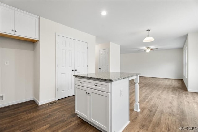 kitchen featuring dark wood-type flooring, white cabinets, ceiling fan, light stone countertops, and a kitchen island