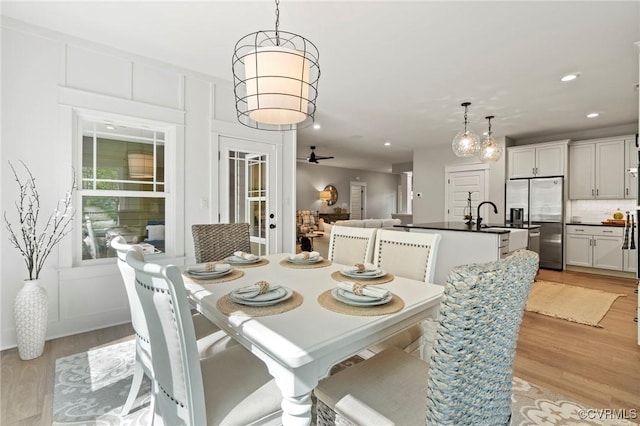 dining area with ceiling fan, light wood-type flooring, and sink