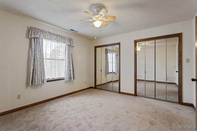 unfurnished bedroom featuring multiple windows, light colored carpet, ceiling fan, and multiple closets