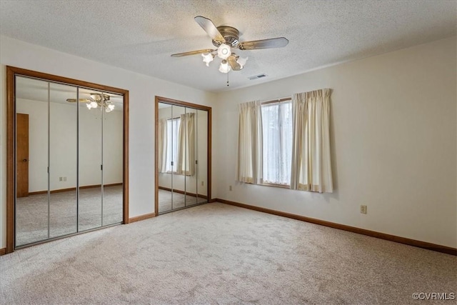 unfurnished bedroom with carpet, a textured ceiling, ceiling fan, and multiple closets