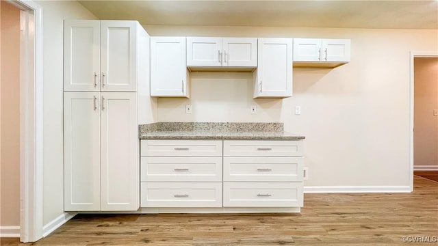 kitchen featuring white cabinets, light wood-type flooring, and light stone counters