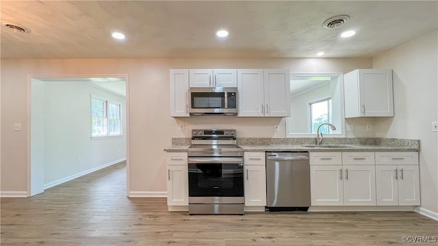 kitchen featuring white cabinets, sink, light hardwood / wood-style flooring, appliances with stainless steel finishes, and light stone counters