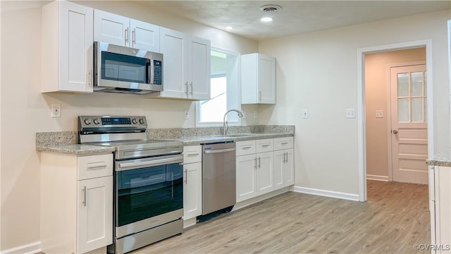 kitchen featuring light hardwood / wood-style floors, white cabinetry, light stone counters, and appliances with stainless steel finishes