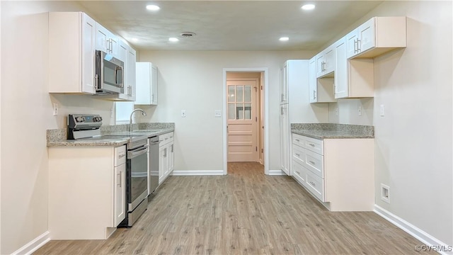 kitchen with light stone counters, white cabinetry, stainless steel appliances, and light hardwood / wood-style flooring