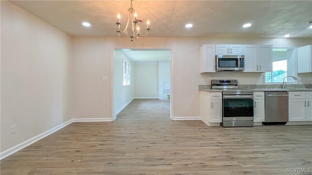 kitchen with white cabinetry, stainless steel appliances, an inviting chandelier, light stone counters, and light wood-type flooring