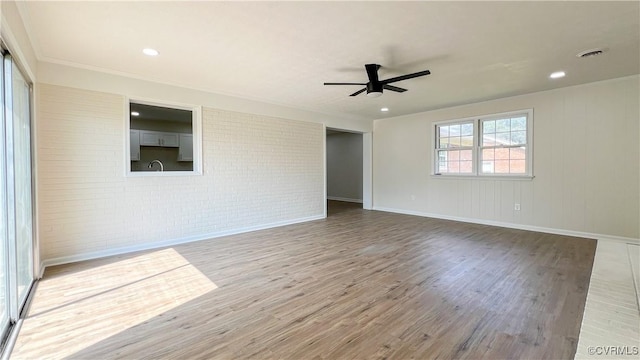 empty room with hardwood / wood-style flooring, ceiling fan, and brick wall