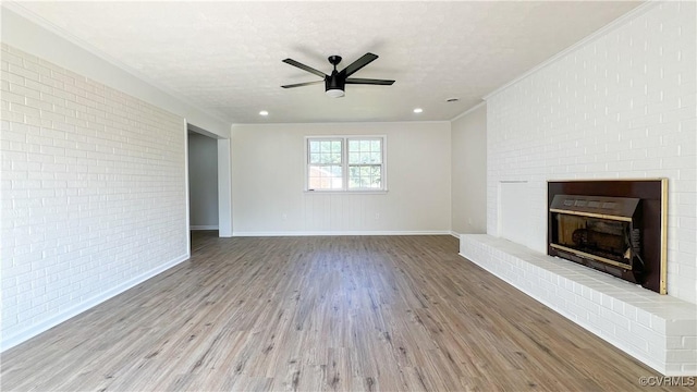 unfurnished living room with ceiling fan, a brick fireplace, light hardwood / wood-style flooring, brick wall, and a textured ceiling