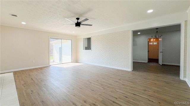 unfurnished room featuring hardwood / wood-style floors, ceiling fan with notable chandelier, and brick wall