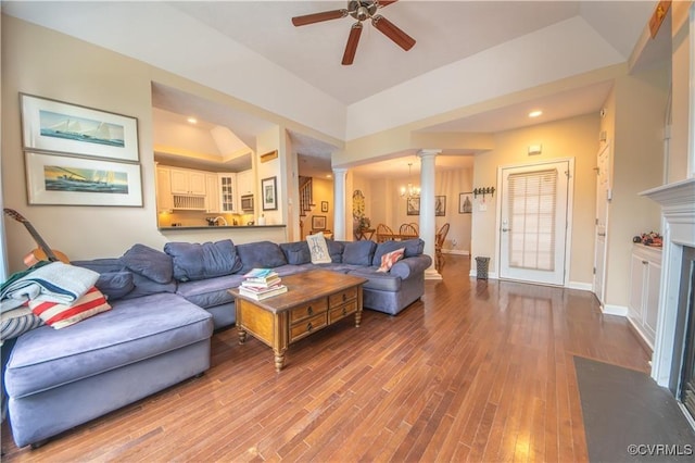 living room featuring decorative columns, ceiling fan with notable chandelier, a raised ceiling, vaulted ceiling, and hardwood / wood-style flooring