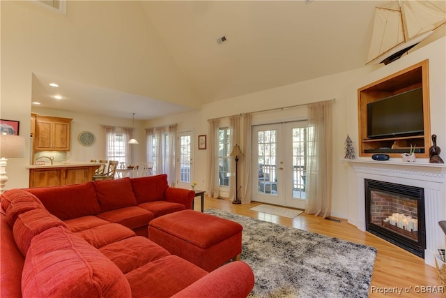 living room featuring french doors, high vaulted ceiling, light hardwood / wood-style flooring, and a healthy amount of sunlight