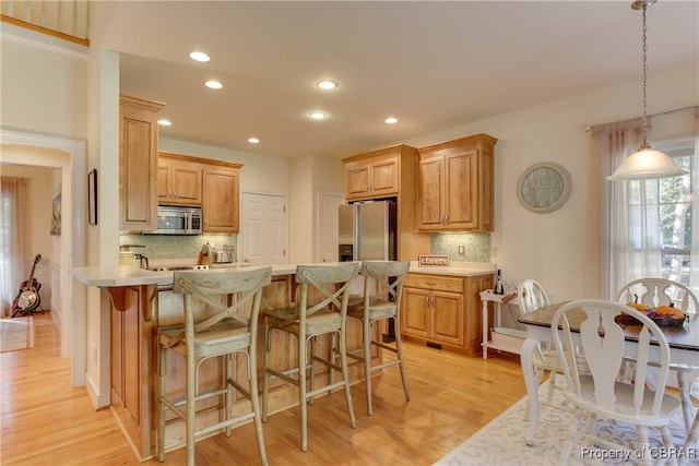 kitchen with hanging light fixtures, stainless steel appliances, tasteful backsplash, light hardwood / wood-style flooring, and a breakfast bar