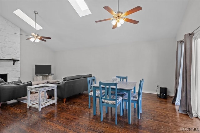 dining room featuring a fireplace, dark hardwood / wood-style flooring, lofted ceiling with skylight, and ceiling fan