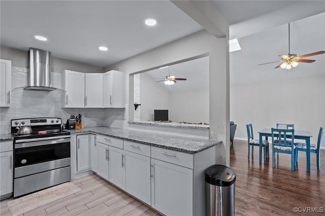 kitchen with stainless steel electric stove, white cabinets, wall chimney range hood, and kitchen peninsula