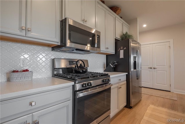 kitchen featuring decorative backsplash, stainless steel appliances, white cabinets, and light hardwood / wood-style floors