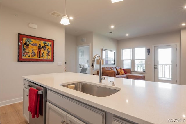 kitchen with stainless steel dishwasher, decorative light fixtures, light wood-type flooring, and sink