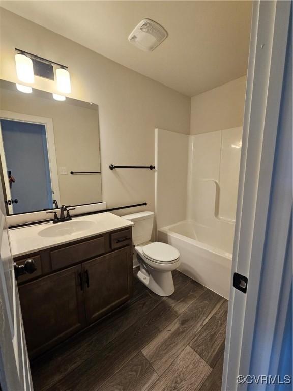 full bathroom with washtub / shower combination, wood-type flooring, vanity, and toilet