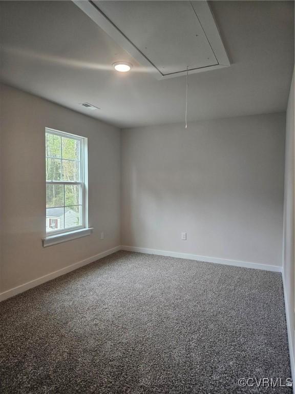 carpeted spare room with attic access, visible vents, and baseboards