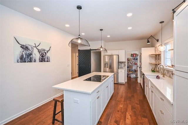 kitchen with pendant lighting, white cabinets, a kitchen island, black electric stovetop, and stainless steel fridge