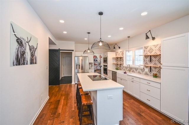 kitchen with appliances with stainless steel finishes, tasteful backsplash, white cabinetry, a barn door, and a kitchen island