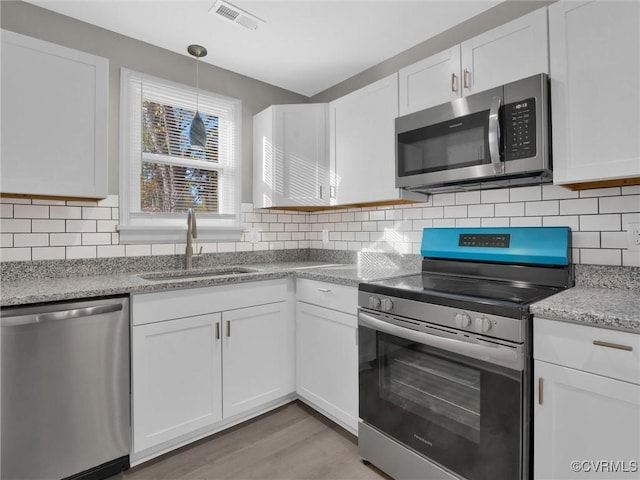 kitchen with white cabinetry, sink, stainless steel appliances, and decorative light fixtures