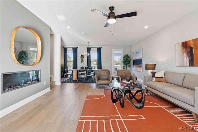 living area with ceiling fan with notable chandelier, recessed lighting, baseboards, and wood finished floors