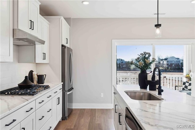 kitchen featuring light stone counters, under cabinet range hood, a sink, appliances with stainless steel finishes, and decorative backsplash