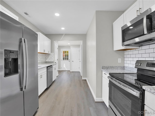 kitchen with tasteful backsplash, white cabinetry, appliances with stainless steel finishes, and light stone counters