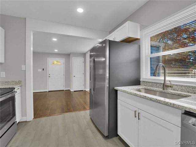 kitchen featuring sink, white cabinets, light hardwood / wood-style floors, stainless steel appliances, and light stone countertops