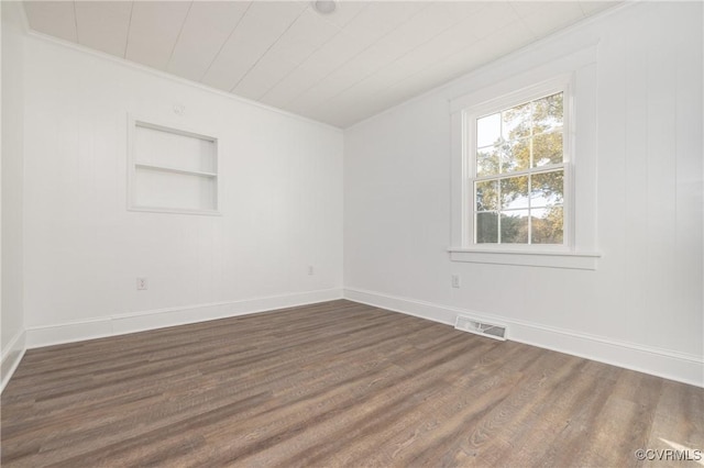 empty room with crown molding, built in features, and dark hardwood / wood-style floors