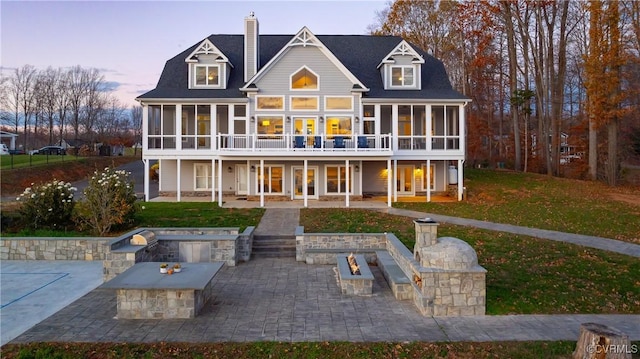 back house at dusk with a patio area, a sunroom, a yard, and a fire pit