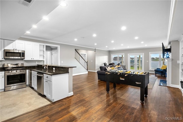 kitchen featuring kitchen peninsula, stainless steel appliances, wood-type flooring, dark stone countertops, and white cabinetry