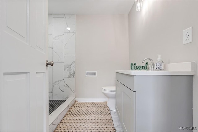 bathroom with tiled shower, vanity, and toilet