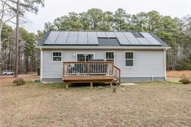 back of property featuring a wooden deck, a yard, and solar panels