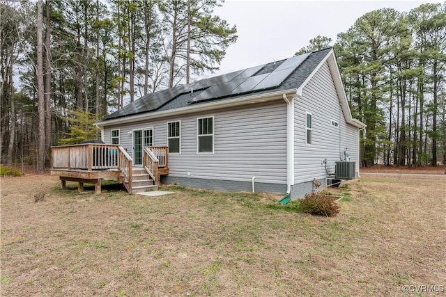 view of front of property featuring central air condition unit, a wooden deck, a front lawn, and solar panels