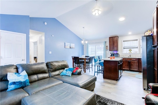 living room featuring ceiling fan with notable chandelier, light wood-type flooring, and vaulted ceiling