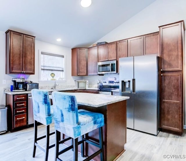 kitchen featuring lofted ceiling, light wood-type flooring, appliances with stainless steel finishes, a kitchen island, and a kitchen bar