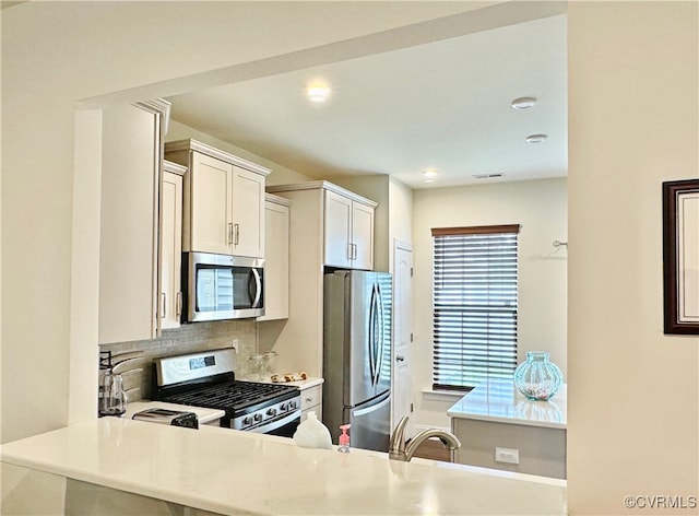 kitchen with sink, stainless steel appliances, backsplash, kitchen peninsula, and white cabinets