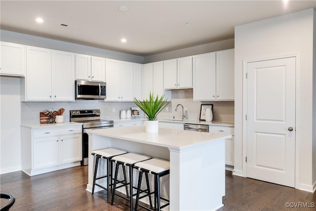 kitchen featuring dark wood-type flooring, a kitchen island, a breakfast bar area, white cabinets, and appliances with stainless steel finishes