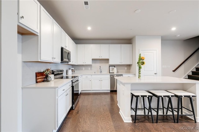 kitchen featuring a kitchen bar, stainless steel appliances, white cabinets, dark hardwood / wood-style floors, and a kitchen island