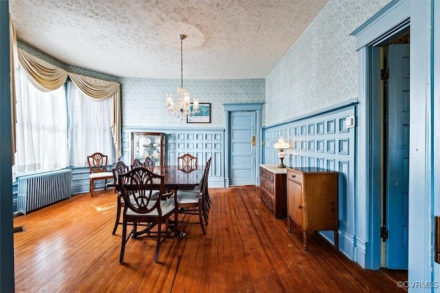 dining room with radiator heating unit, a textured ceiling, a notable chandelier, and hardwood / wood-style floors