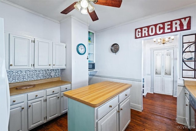 kitchen featuring a center island, dark wood-type flooring, white cabinets, ceiling fan with notable chandelier, and ornamental molding