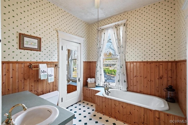 bathroom with a bathing tub, vanity, a textured ceiling, and wooden walls