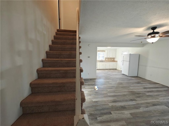 stairway with hardwood / wood-style flooring, ceiling fan, and a textured ceiling