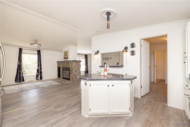 kitchen with dark stone counters, light hardwood / wood-style flooring, a center island, white cabinetry, and a stone fireplace